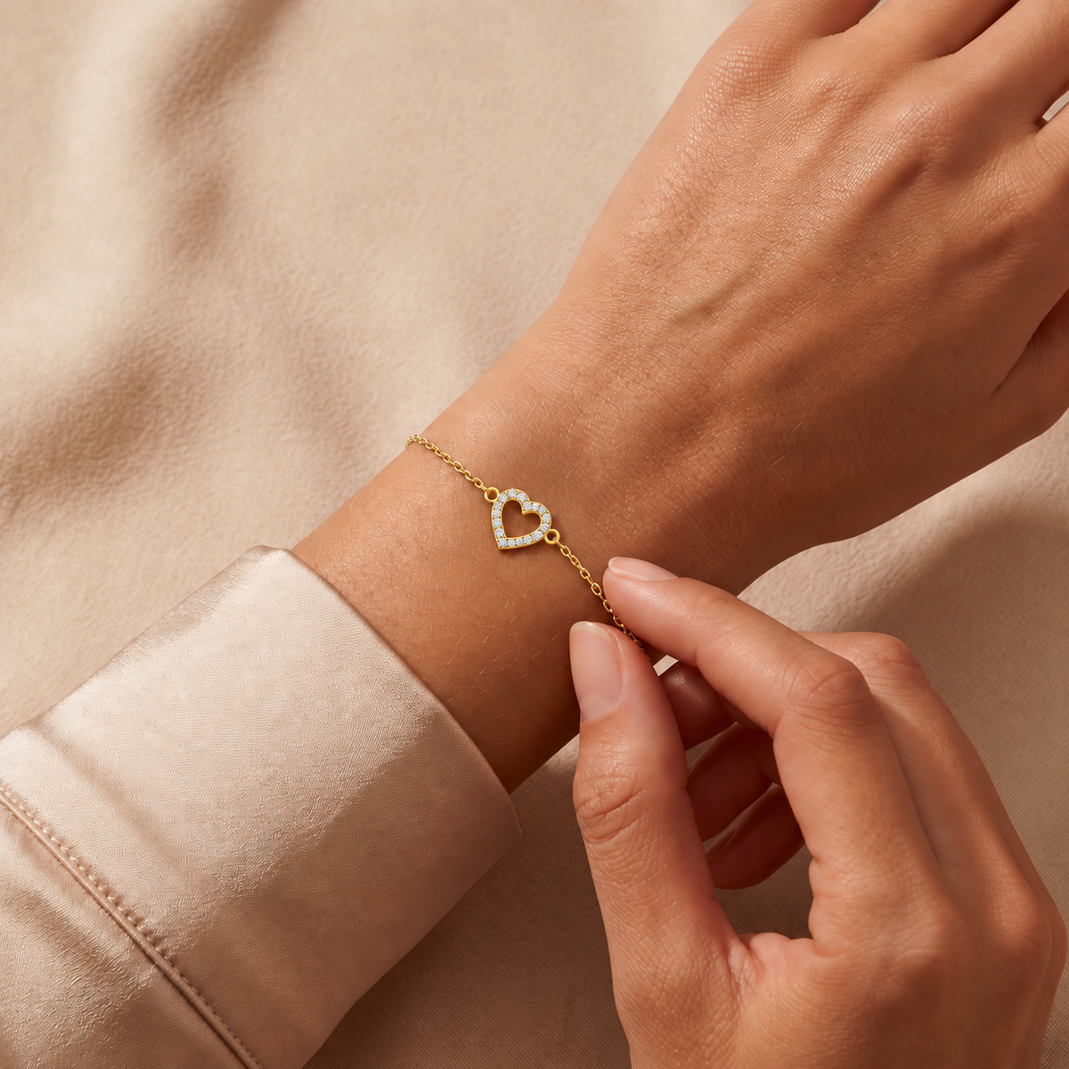 Yellow gold open pave heart diamond bracelet 105-10005 worn on a wrist against champagne satin and beige fabric