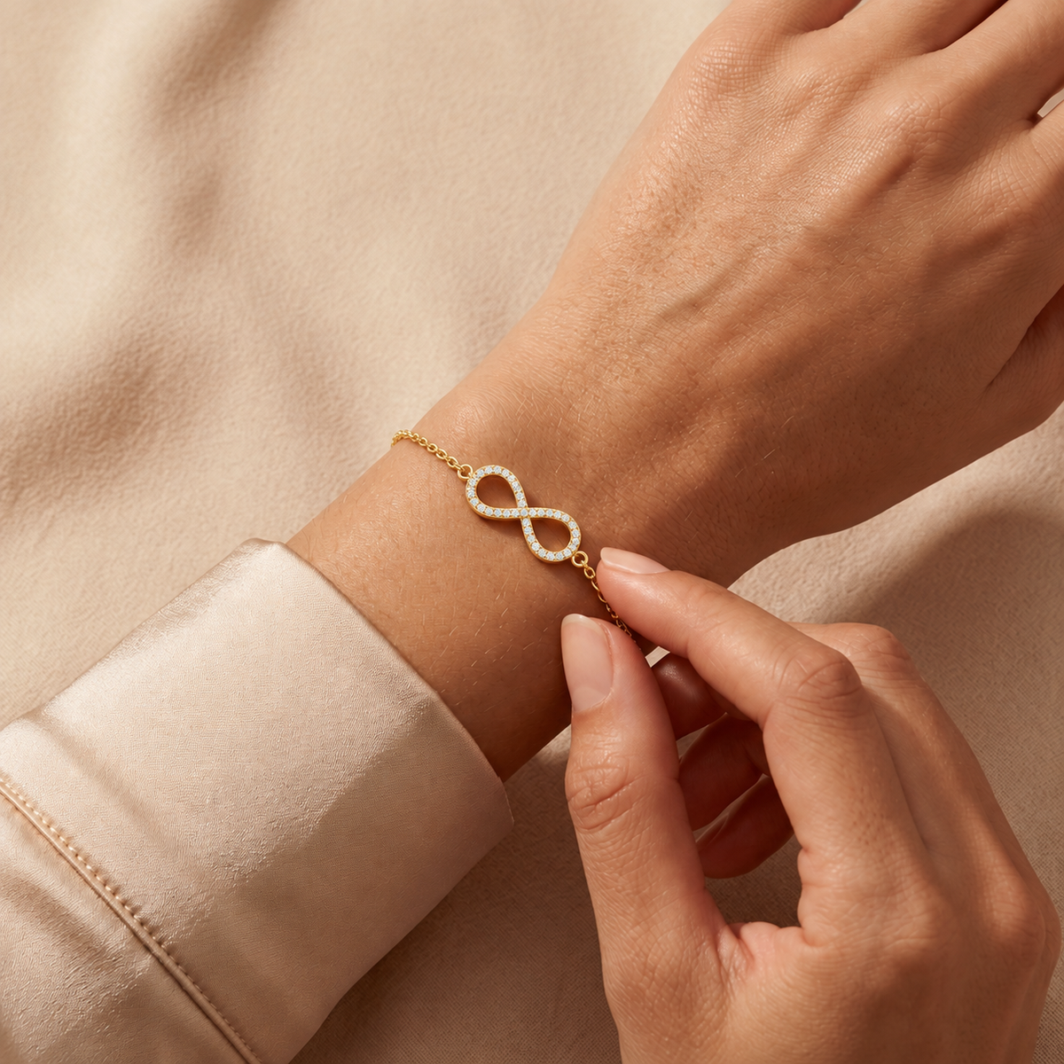 Yellow gold full pave infinity diamond bracelet 105-10006 worn on a wrist against champagne satin and beige fabric