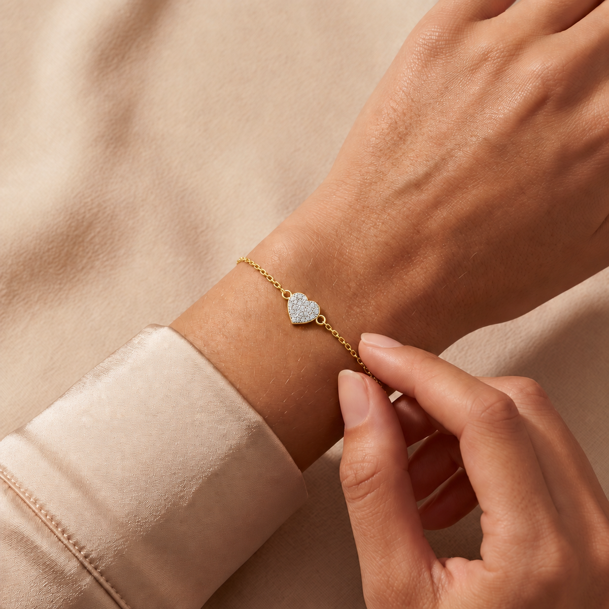 Yellow gold pave heart diamond bracelet 105-10012 worn on a wrist against champagne satin and beige fabric