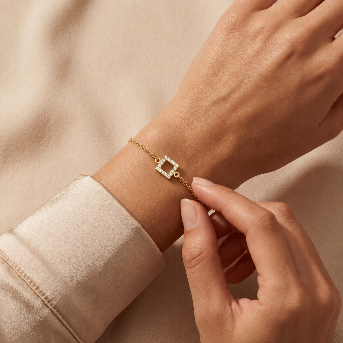 Yellow gold open pave square diamond bracelet 105-10016 worn on a wrist against champagne satin and beige fabric